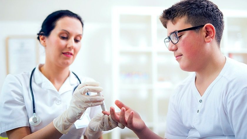 A healthcare worker checking the blood glucose level of a teenage patient by pricking their fingertip